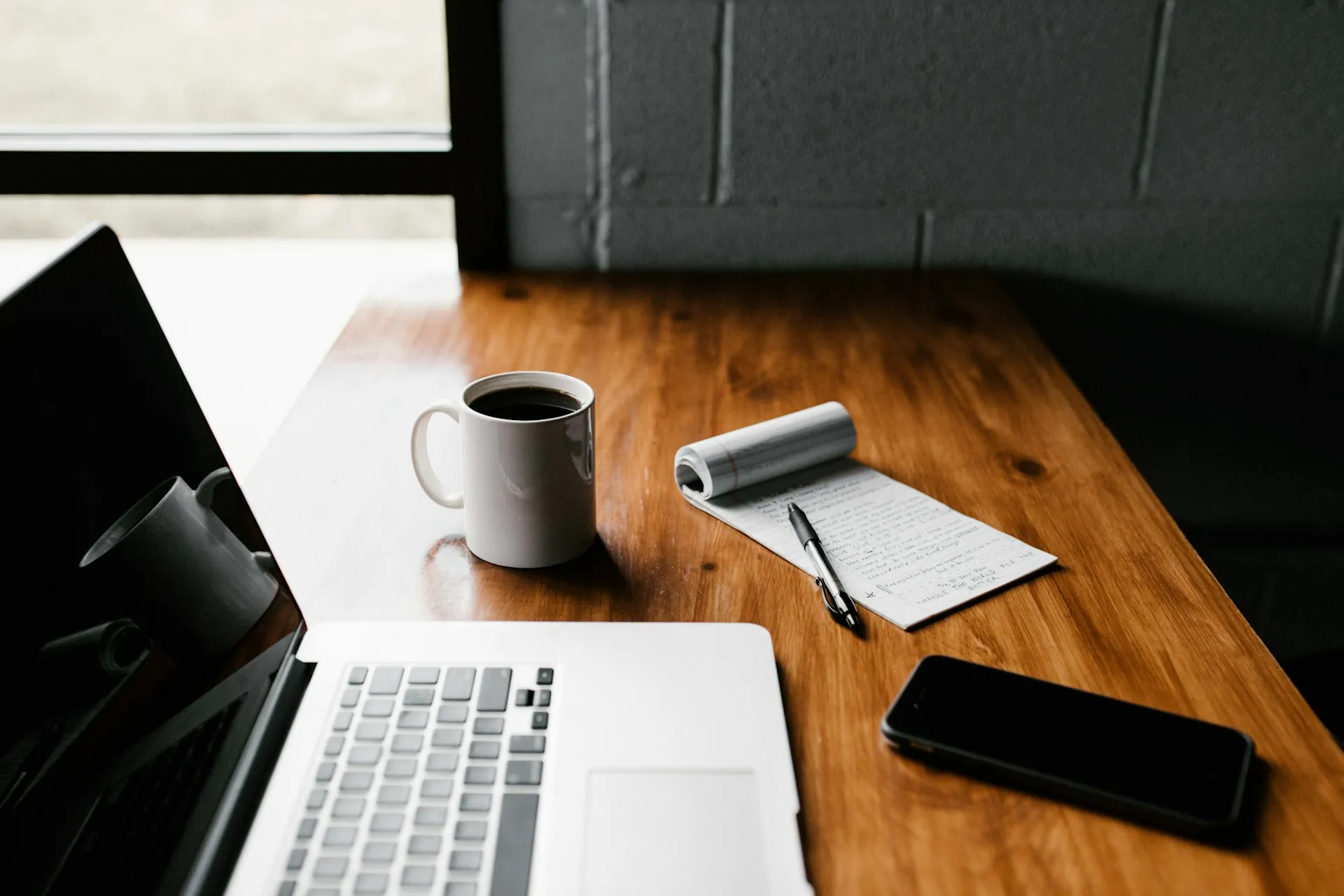A laptop placed on a wooden table next to a cup of coffee and a phone. Photo by Andrew Neel on Unsplash